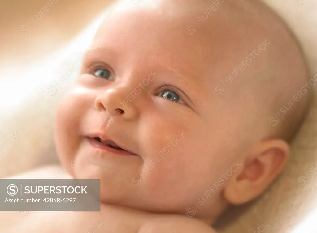 Close up of a young infant smiling and looking toward a bright light.