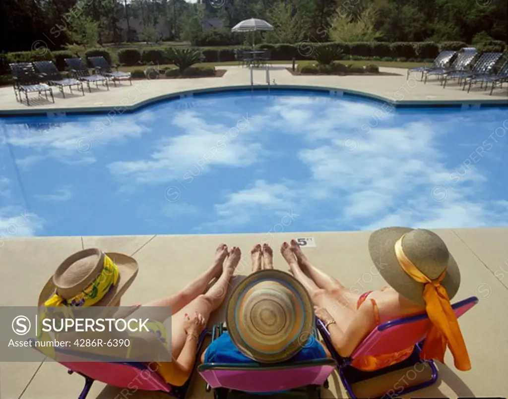 Women sunbathing at pool with reflections of clouds in the water