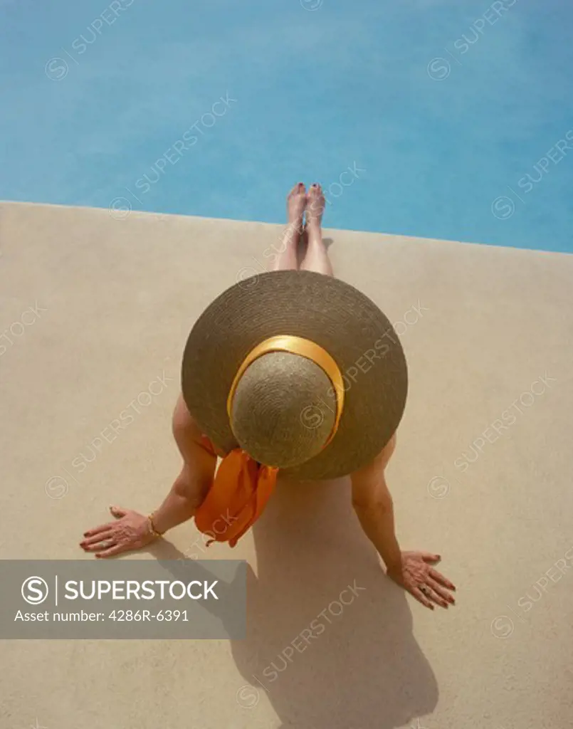 Birdseye view of woman sitting by pool in wide brim sun hat