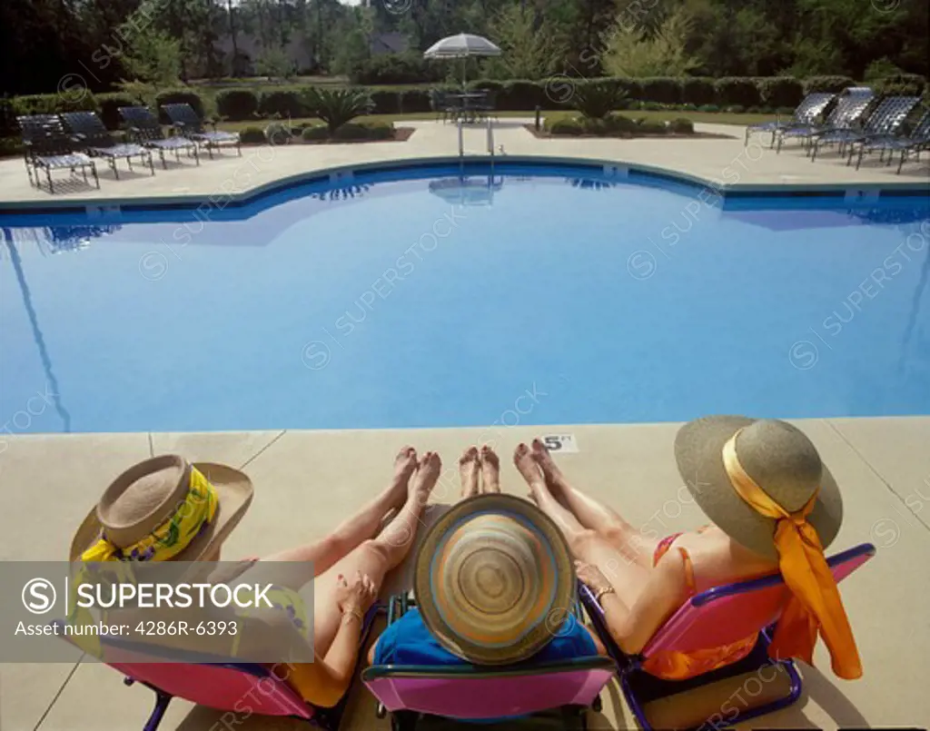 Birdseye view of three women sitting at pool wearing wide brim sun hats