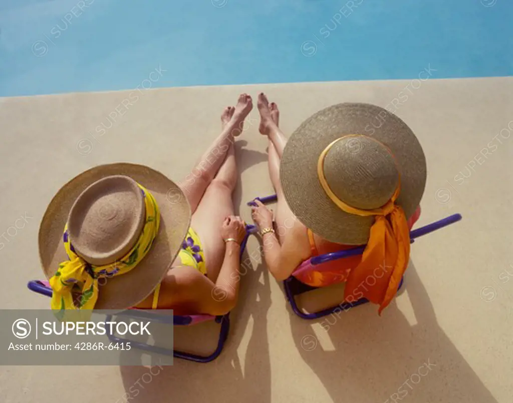 Birdseye view of two women sitting by pool in wide brim colorful straw hats