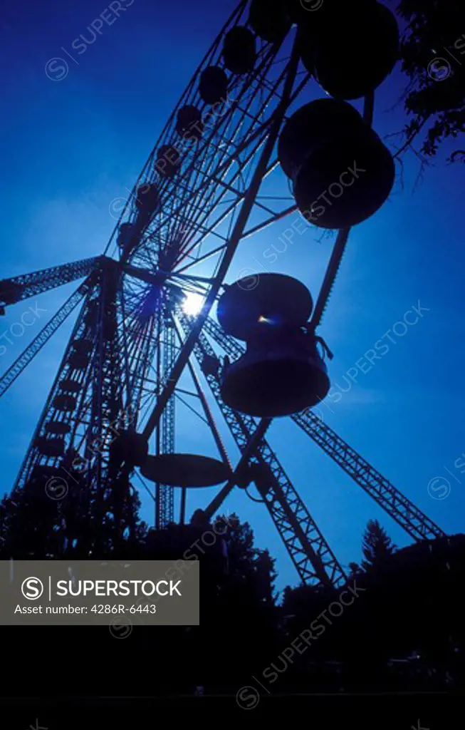 A silhouette of a ferris wheel in motion at dusk against a blue sky