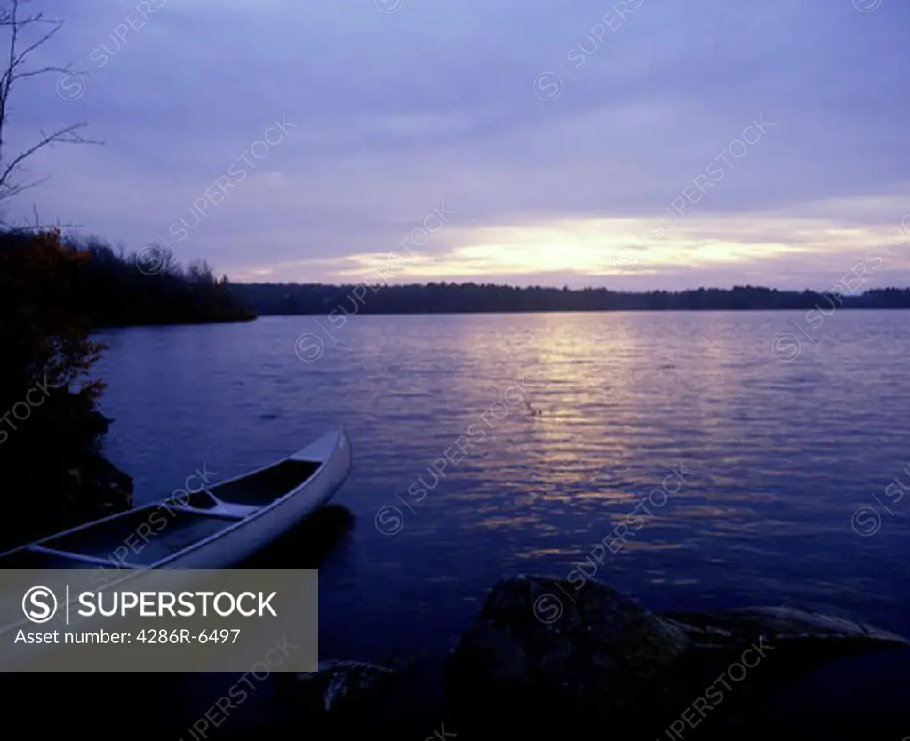 Scenic of a canoe docked on still lake at sunrise or sunset