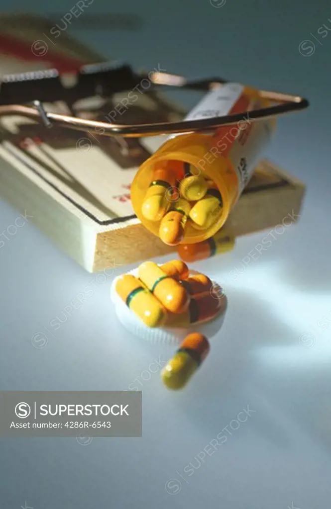 A still life of an open pill container caught in a mouse trap.