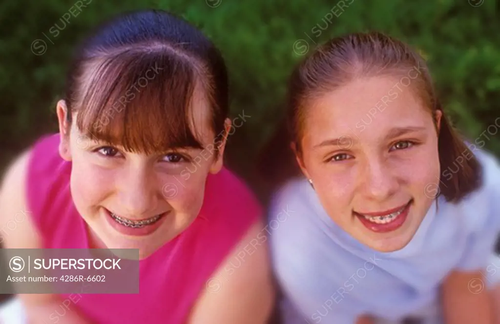 Two young teenage girls with braces smiling while looking up at camera