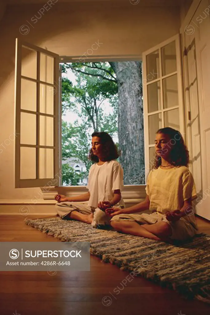 A teenage girl and her mother doing yoga postures in front of a window.