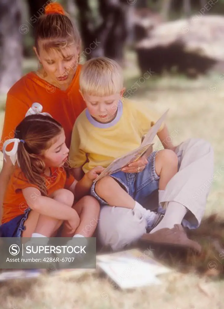 A mother and her children sitting under a tree reading a book.