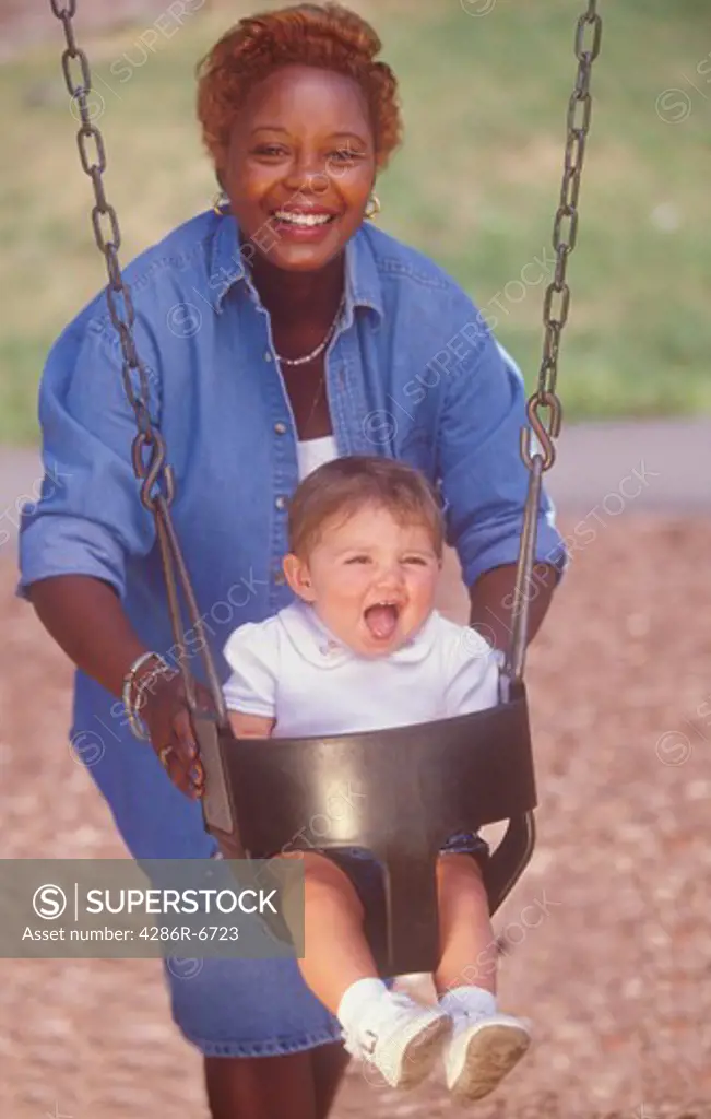 A daycare worker pushing a young child in a swing.