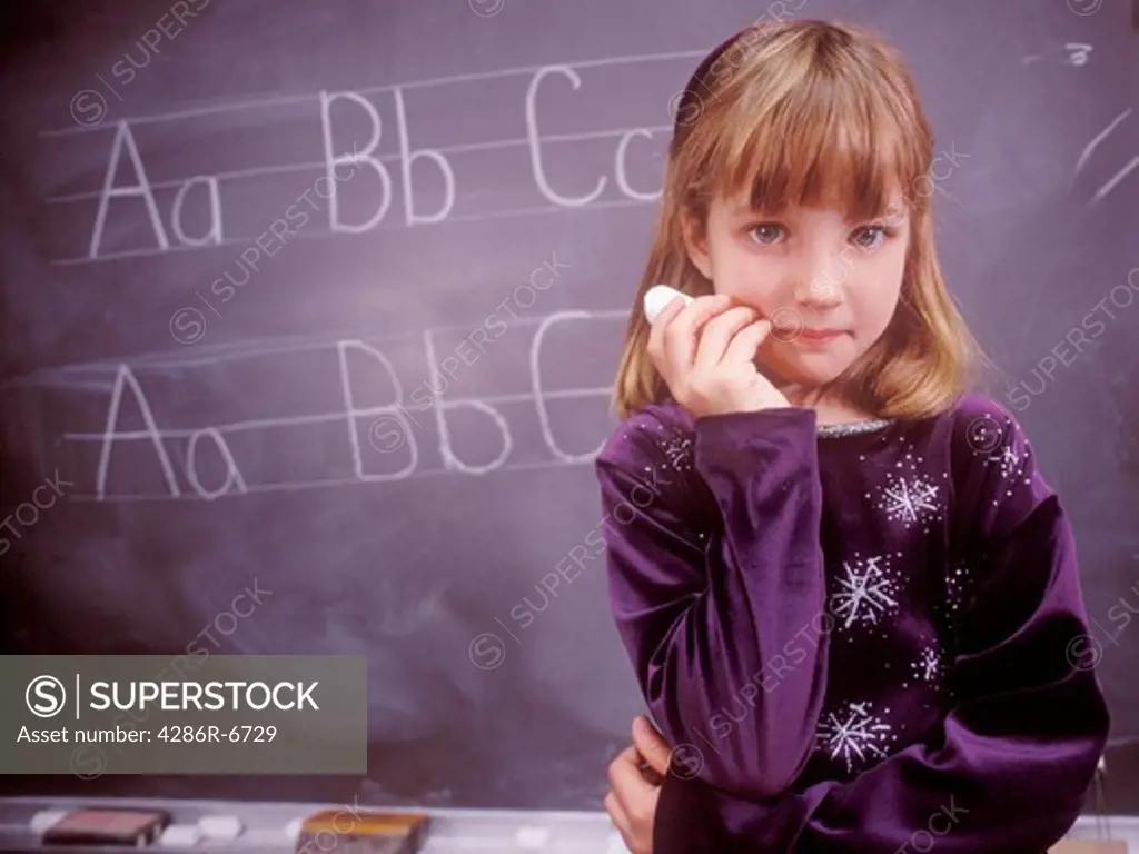 A pensive young female student holding a piece of chalk and looking at the camera.