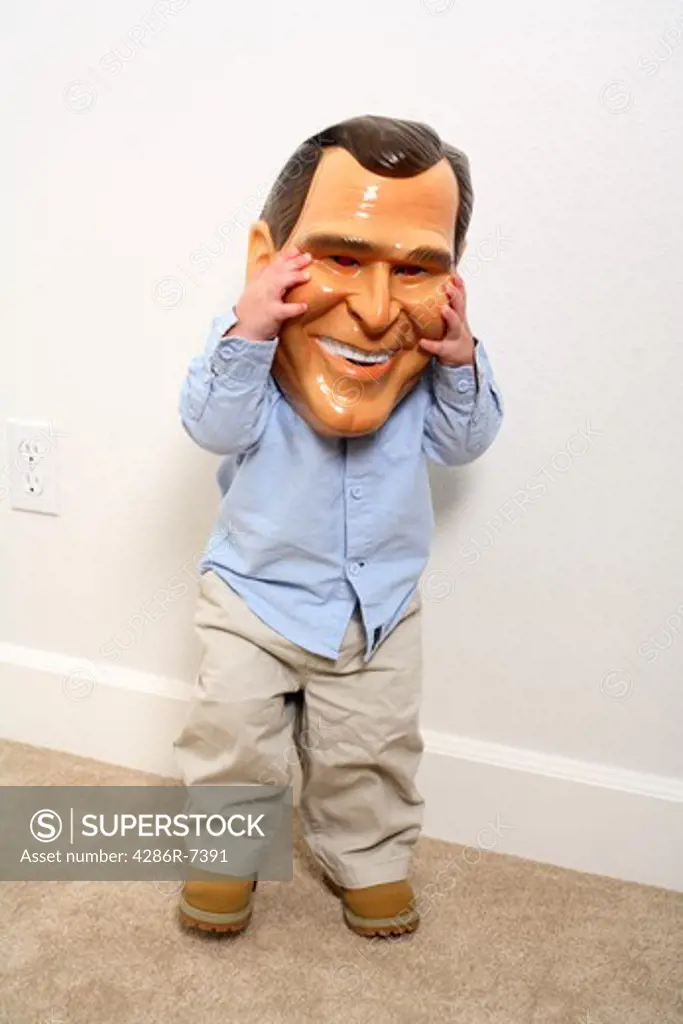 Toddler holding George Bush mask over face