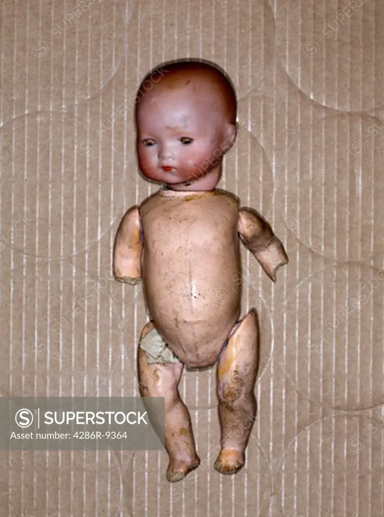 An abused naked doll sits in a cardboard box.