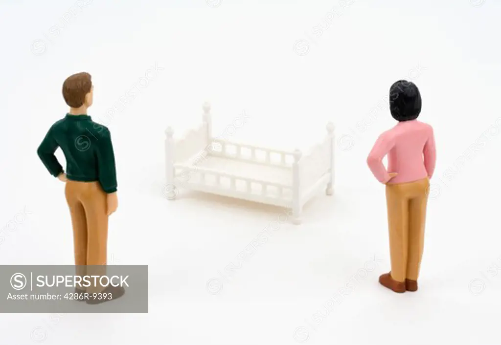 Man and woman figurines look at a bed.