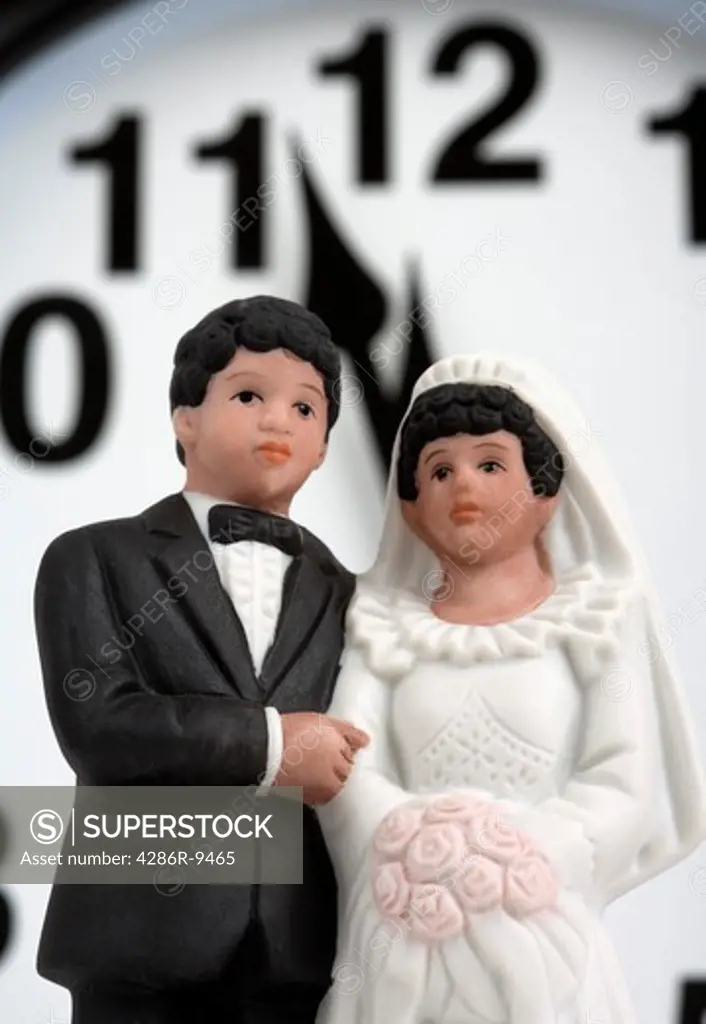 Bride and groom figurines in front of midnight or noon on a clock.