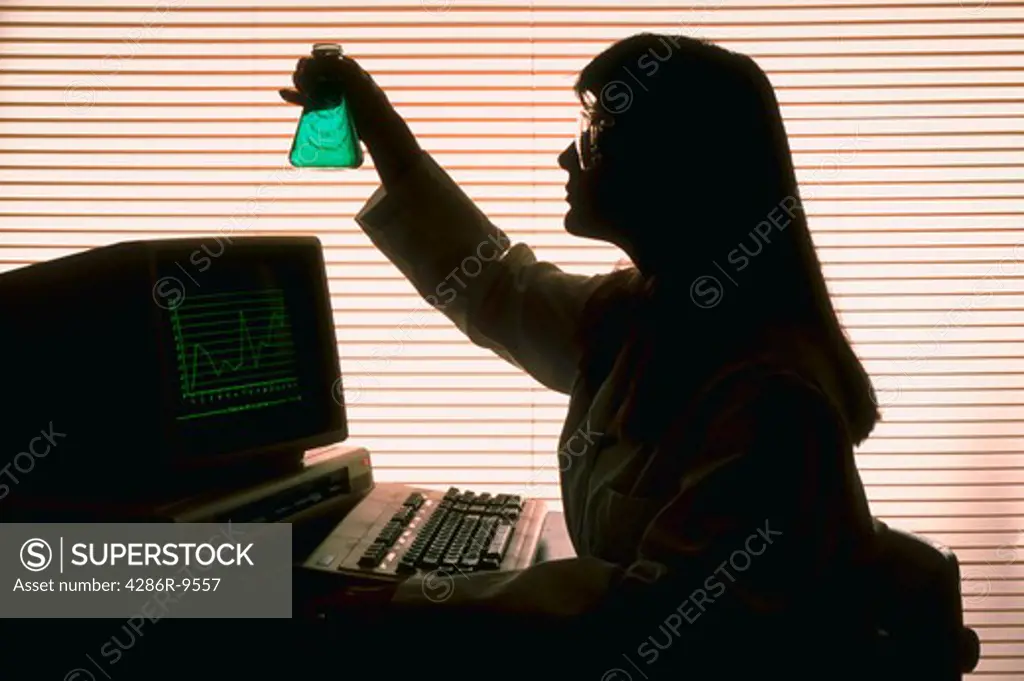Silhouette of woman with beaker at computer
