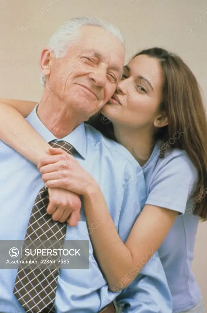 MIddle aged business man with his daughter embracing him and kissing him on the cheek.
