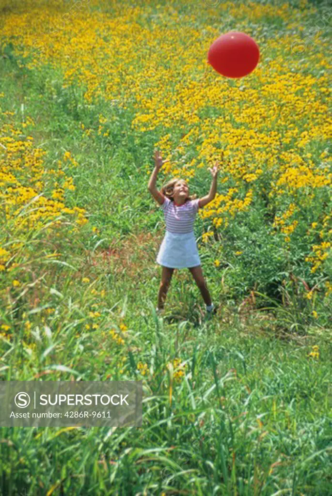 Young girl holding a balloon while standing in a field of flowers.
