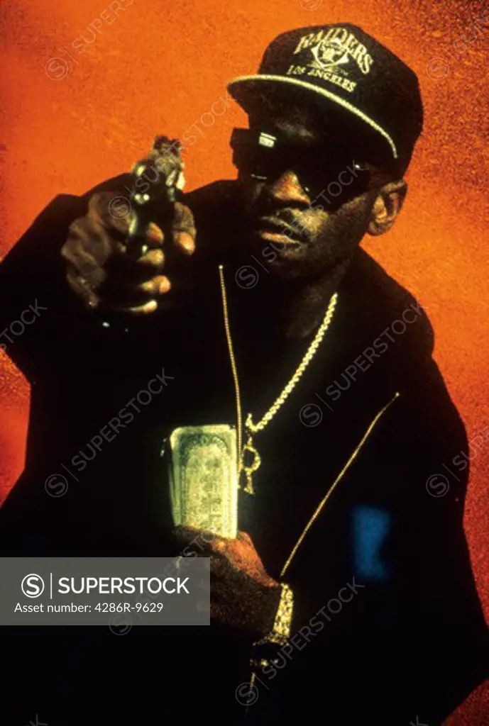 African-American man aiming a gun at the camera and holding money in his other hand depicting violence and crime.
