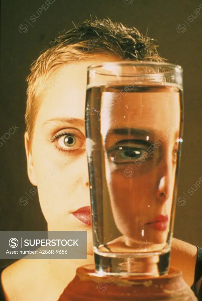 Close-up of a womans face being refracted by a glass of water.