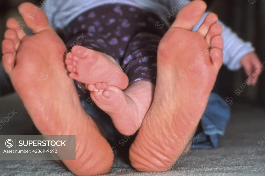 Close-up view of an adults pair of feet and the childs feet nestled in between.