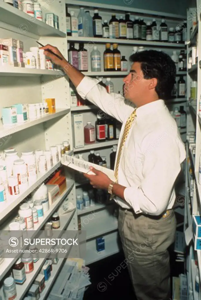 A male phatmacist taking an inventory count of the different medicines on the shelf.