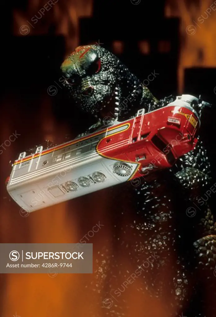 Generic lizard monster toy destroying a subway car with simulated fire all around it.