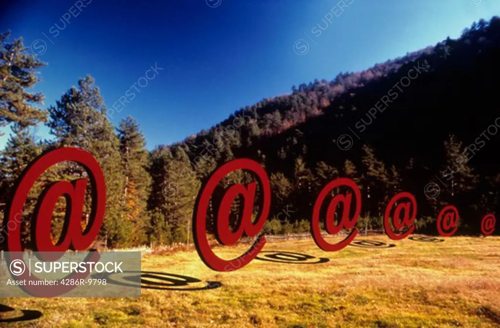 Digitally manipulated image of the email @ sign lined up in a row outdoors in a mountain landscape.