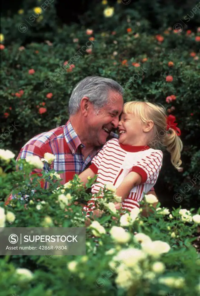 Grandfather and granddaughter smiling and enjoying each others company while outdoors surrounded by flowers.