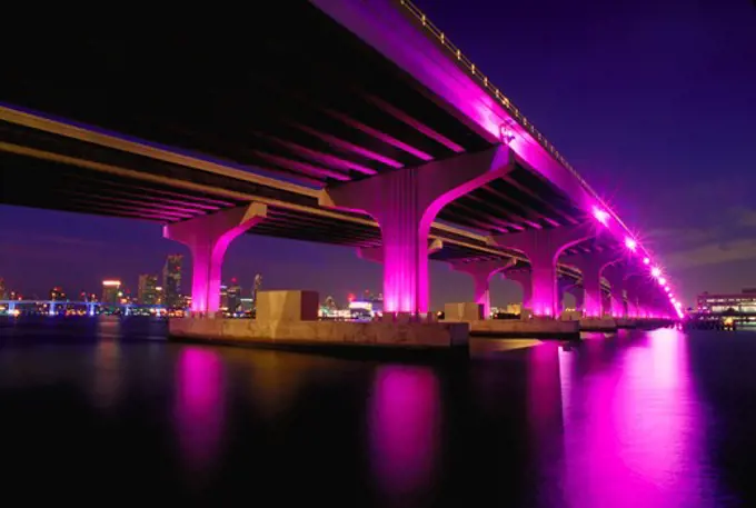 Rickenbaker Causeway bridge over Biscayne Bay in Miami, Florida as magenta lights illuminate the bridge as part of a beautification project.
