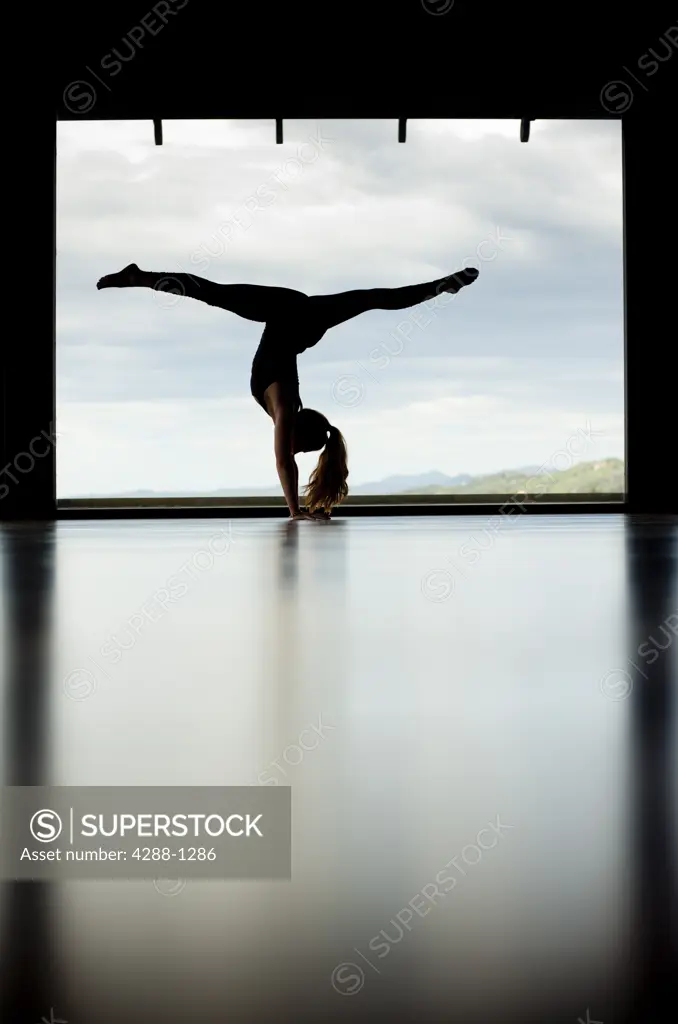 Woman performs handstand in front of large window.