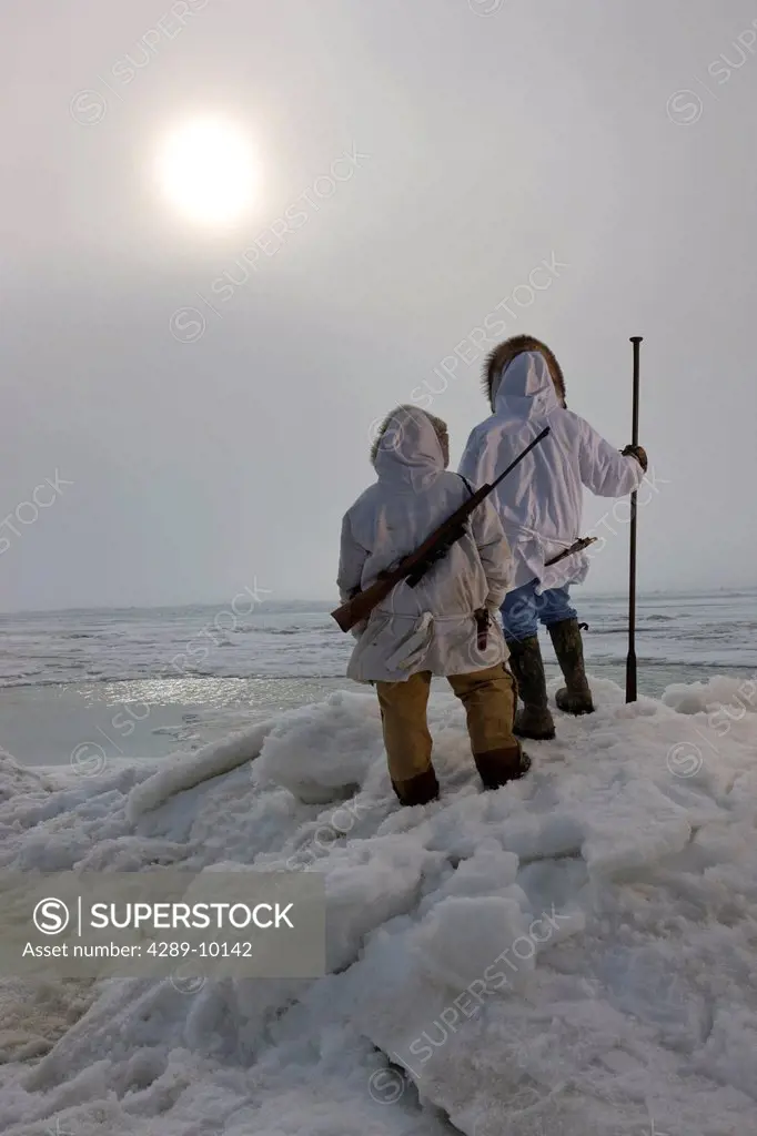 Male and female Inupiaq Eskimo hunters wearing their Eskimo parka´s Atigi carry a rifle and walking stick while looking out over the Chukchi Sea, Barr...