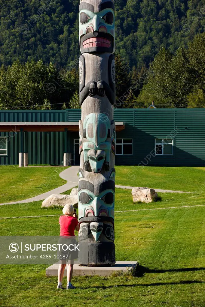 Tourist taking a photo of the Tlinget Totem Pole at the Haines Public school, Southeast Alaska, Summer