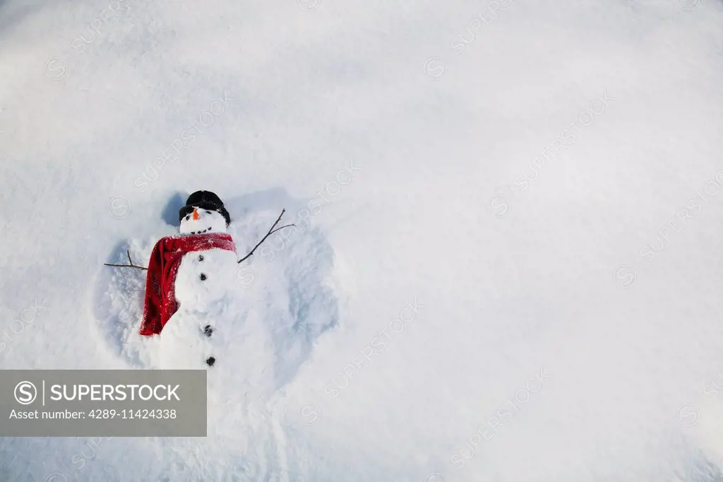 Snowman wearing a red scarf and black top hat making snow angels in the snow, Russian Jack Springs city park, Anchorage, South Central Alaska, Alaska,...