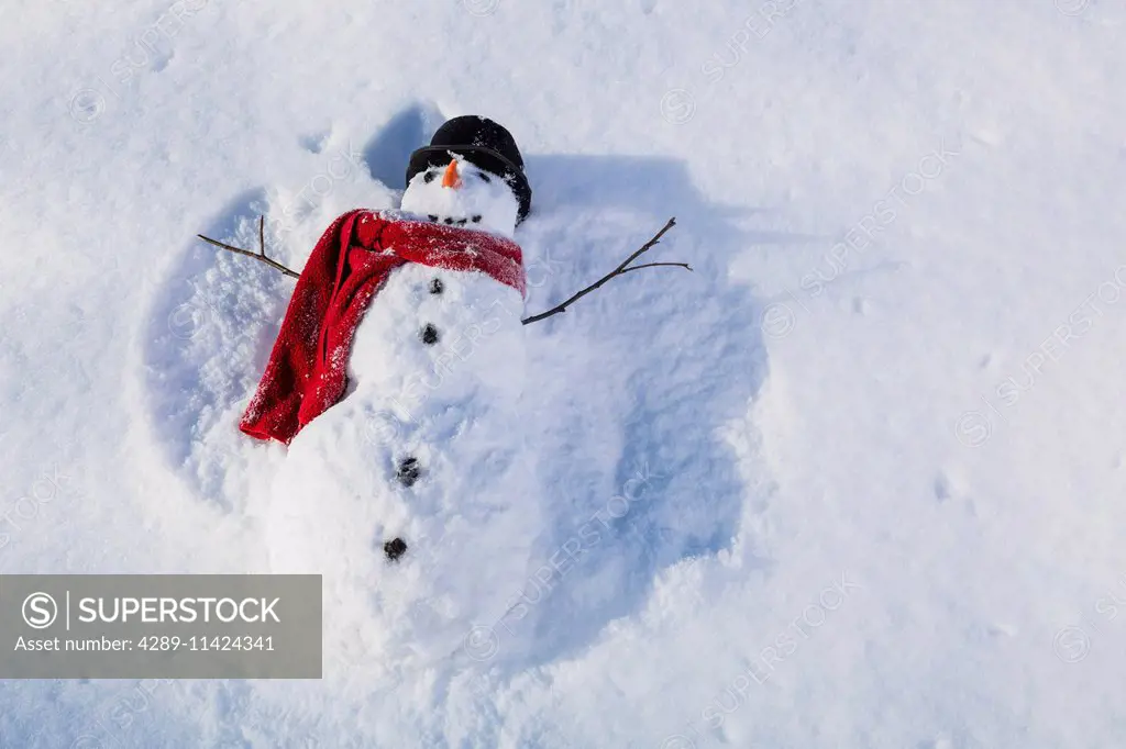 Snowman wearing a red scarf and black top hat making snow angels in the snow, Russian Jack Springs city park, Anchorage, South Central Alaska, Alaska,...