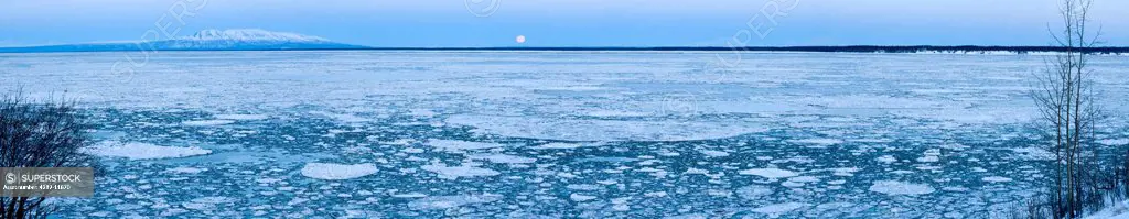Panoramic view of the full moon setting behind Mt. Susitna and ice in Cook Inlet, Point Woronzof, Anchorage, Southcentral Alaska, Winter