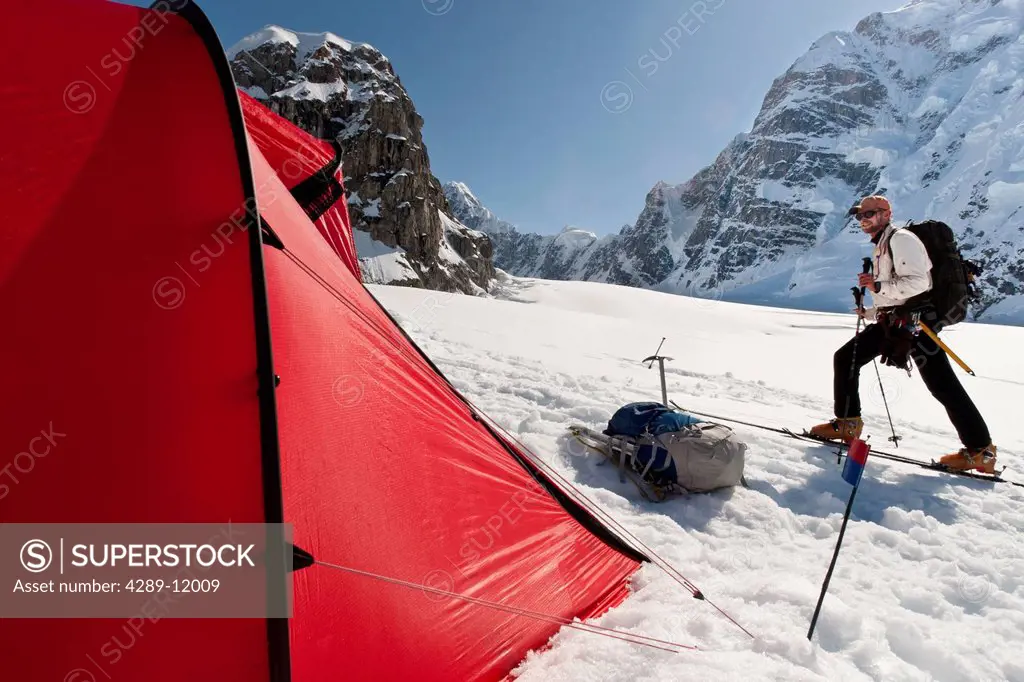 Man skiing by a red tent on the Kahiltna Glacier in the Alaska Range, Interior Alaska, Summer