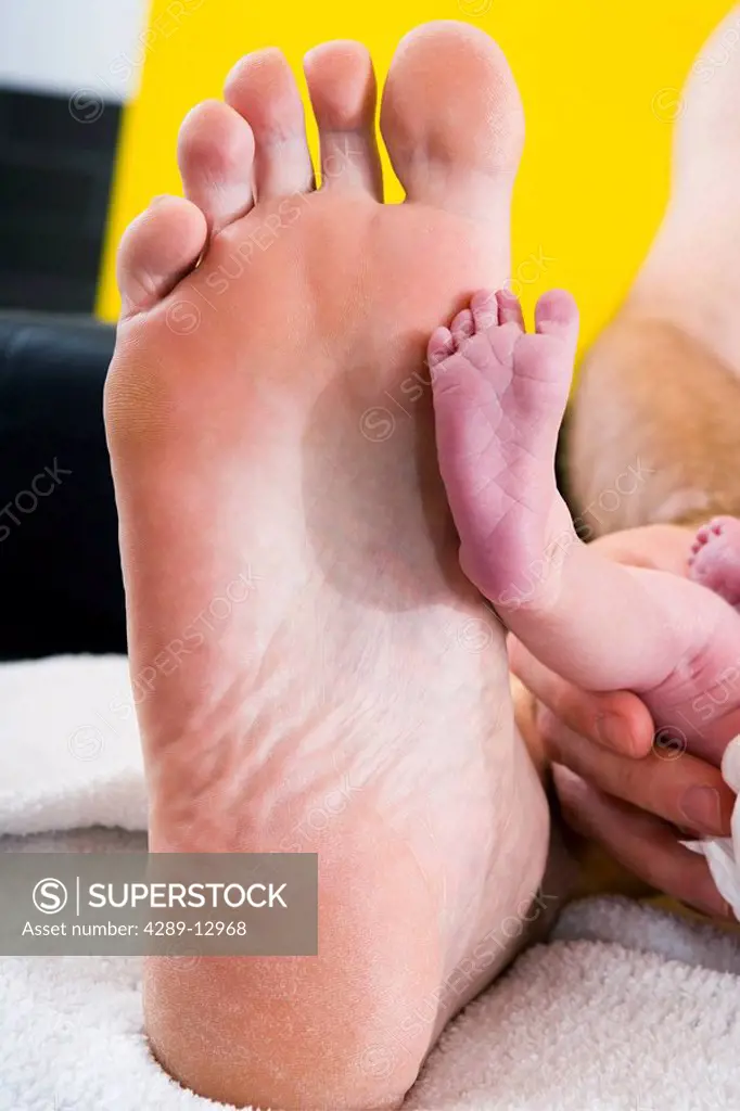 Newborn infant´s foot placed in front of man´s foot for size comparison lying on a white blanket Alaska United States