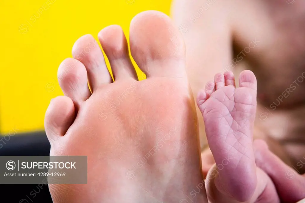 Newborn infant´s foot placed in front of man´s foot for size comparison lying on a white blanket Alaska United States