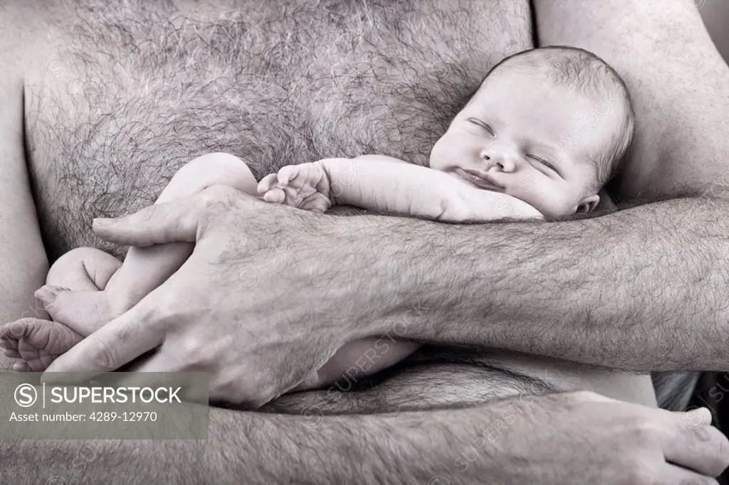 Close up of sleeping newborn infant being held against a man´s bare chest nesteled in his arms Alaska United States
