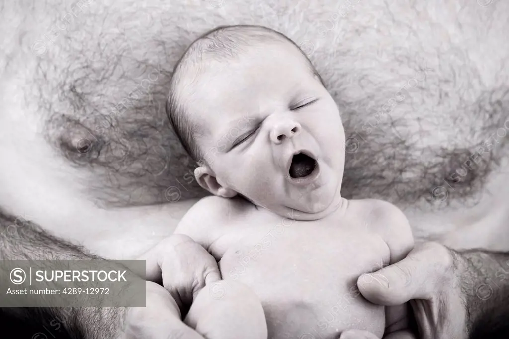 Close up of sleeping newborn infant being held against a man´s bare chest nesteled in his arms Alaska United States