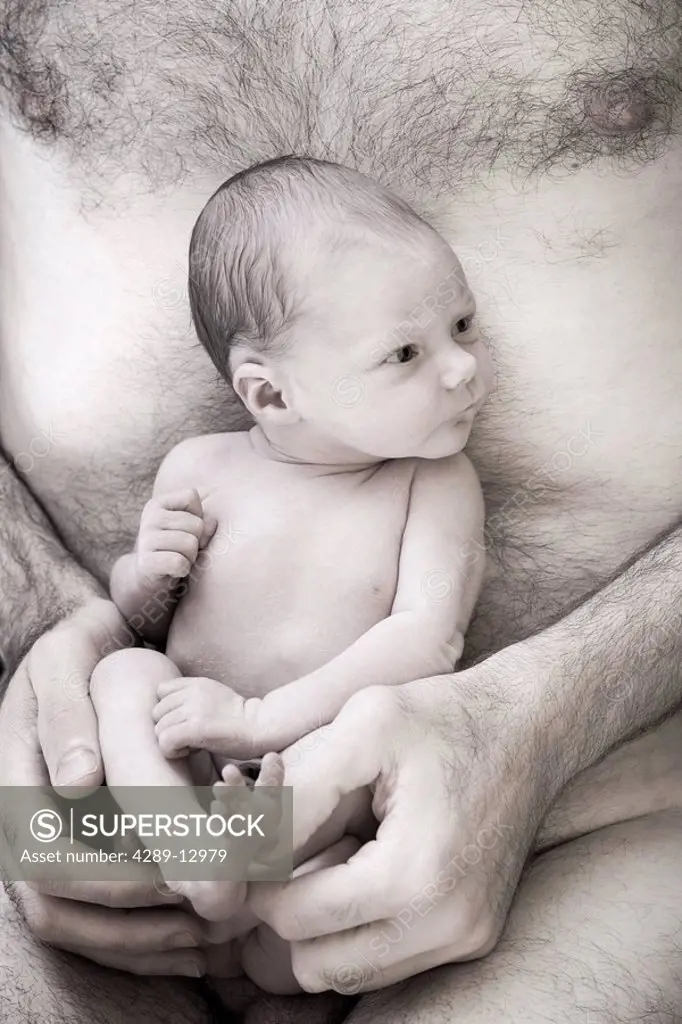 Close up of man holding a awake newborn infant in his hands against his bare chest Alaska United States