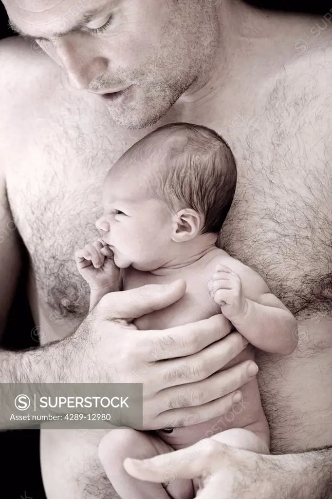 Close up of man holding an awake newborn infant in his hands against his bare chest Alaska United States