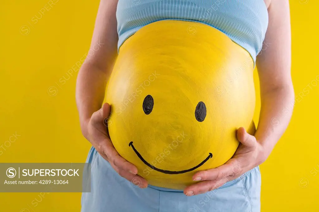 View of pregnant woman´s belly with yellow Smiley Face painted on her stomach Alaska United States
