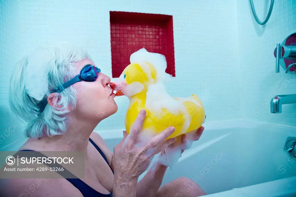 Senior woman having some fun in the tub with a yellow rubber duck wearing swim goggles