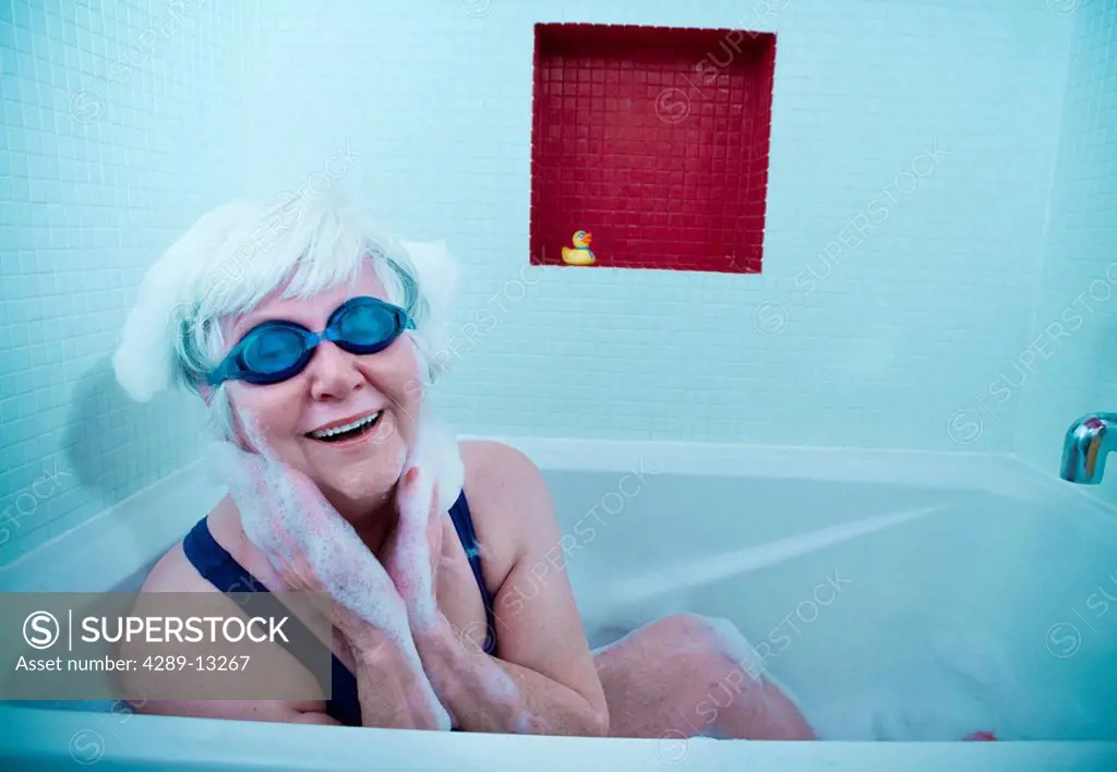 Senior woman having some fun in the tub with a bath bubbles & wearing swim goggles