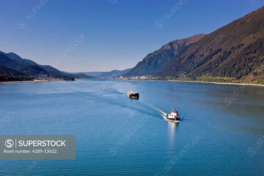 Aerial view of a tugboat towing a cargo ship out of Lynn canal, Mount Roberts and downtown Juneau in the background, Southeast Alaska, Summer