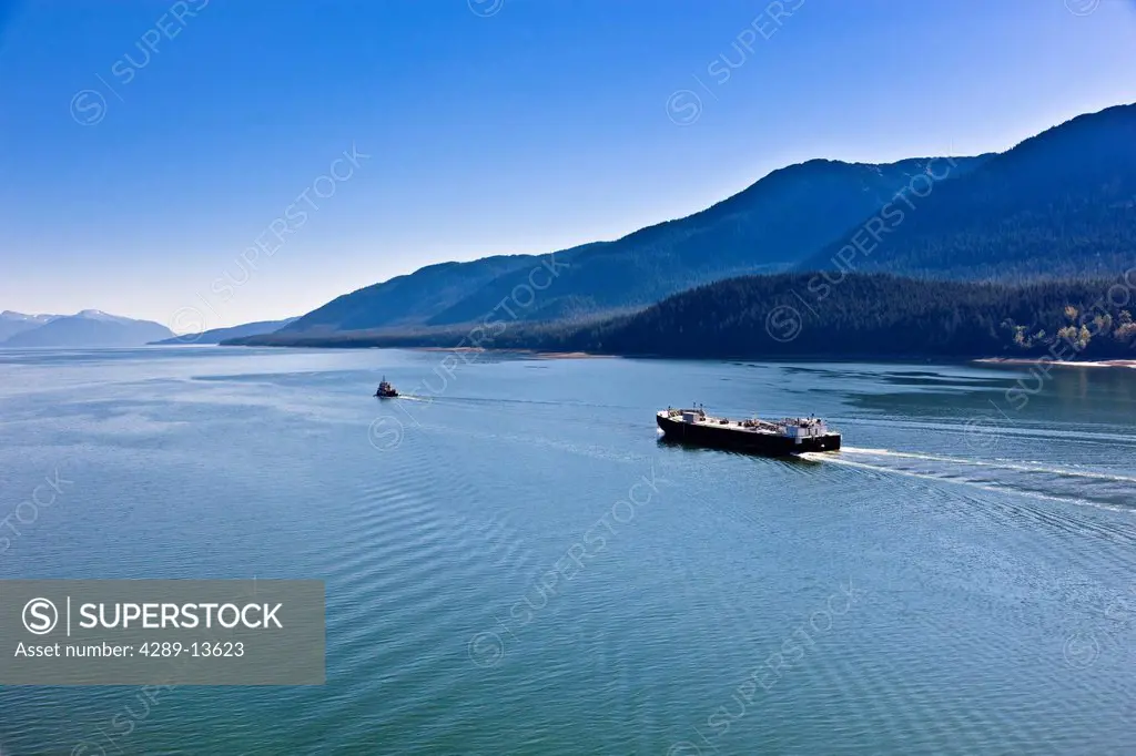 Aerial view of a tugboat towing a cargo ship out of Lynn canal, Mount Roberts and downtown Juneau in the background, Southeast Alaska, Summer