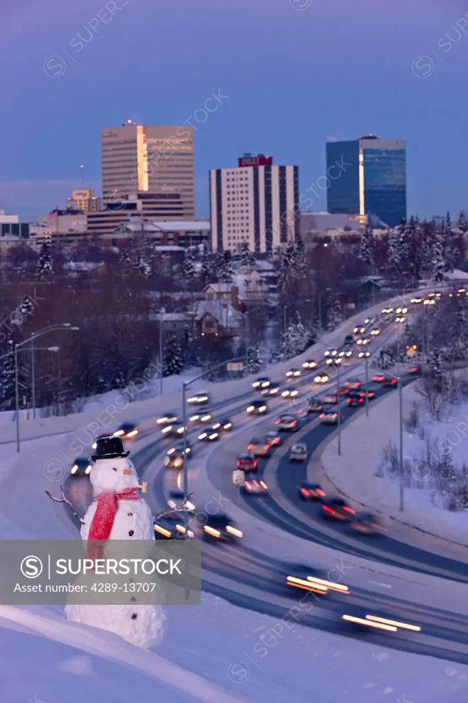 View of traffic and downtown Anchorage with a snowman in the foreground, Southcentral Alaska, Winter. Digitally altered.