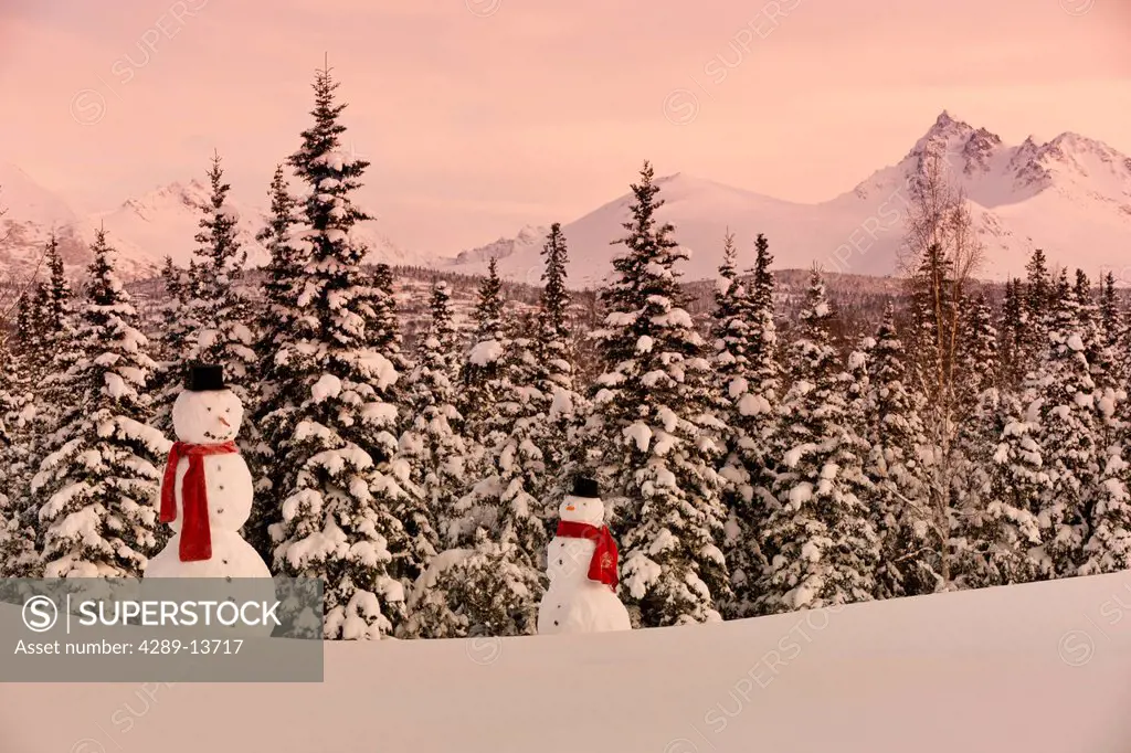 Scenic view of Chugach Mountains with an adult and child snowmen wearing a scarf and top hat in the foreground, Anchorage, Southcentral Alaska, Winter