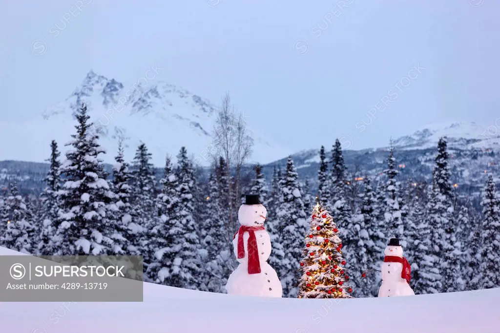 Photo of adult and child snowmen wearing red scarves and black top hats standing next to a Christmas tree with red ornaments in front of a snowcovered...