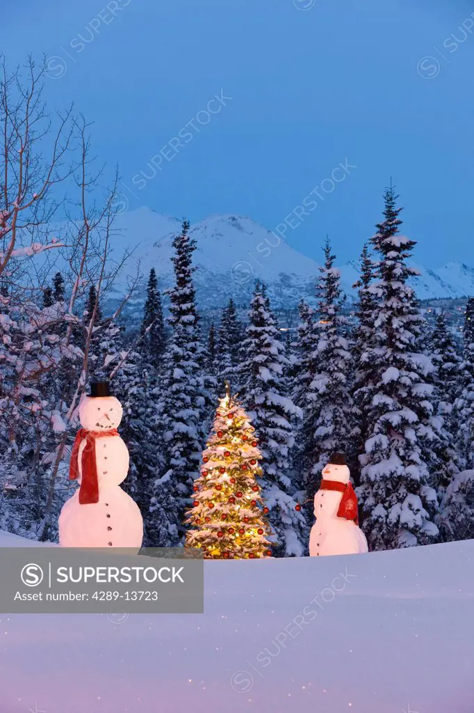 Photo of adult and child snowmen wearing red scarves and black top hats standing next to a Christmas tree with red ornaments in front of a snowcovered...